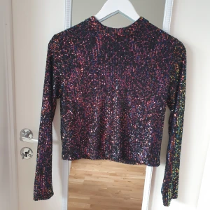 Svart/ multifärgad paljettopp från Mango - Säljer en glittrig svart topp från Mango, täckt med färgglada paljetter som ger en festlig look. Toppen har långa ärmar och en dragkedja i ryggen för enkel påklädning. Perfekt för att lysa upp kvällen! ✨