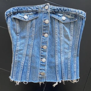 Jeanskorsett topp - Snygg jeanskorsett från Zara med knappar framtill och fransig nederkant. Den har en elastisk baksida för bättre passform och dekorativa fickor framtill. Perfekt för en trendig look!
