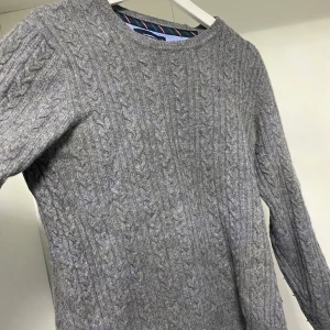 Grå stickad tröja - Säljer en stilren grå stickad tröja med kabelstickat mönster. Tröjan har långa ärmar och en rund halsringning, perfekt för kyligare dagar. Passar till jeans för en avslappnad look.