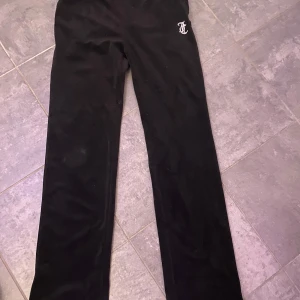 Svarta byxor från Juicy Couture - Snygga svarta byxor från Juicy Couture med glittrande text på baksidan. Perfekta för en avslappnad och stilren look. Byxorna har en bekväm passform och är tillverkade i ett mjukt material. Dock har resåren på kanten snurrat dig. 