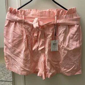 Rosa shorts med knytband - Snygga rosa shorts från ADPT med ett knytband i midjan för en justerbar passform. De har en högmidjad design och är perfekta för varma sommardagar. Shortsen har en mjuk och bekväm känsla. Priset går att diskutera! 