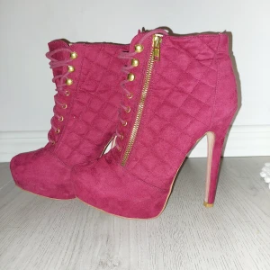 Rosastövletter med klack från just fab - Snygga rosa stövletter i mocka med hög klack och quiltad design. De har snörning och en praktisk dragkedja i guld på sidan för enkel på- och avtagning. Perfekta för att ge en färgklick till din outfit. Använda en gång!