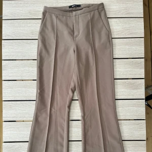 Beige kostymbyxor - Snygga beige kostymbyxor med mid midja och bootcut-stil i storlek S. Använda ett fåtal gånger. Köpta från Gina Tricot.