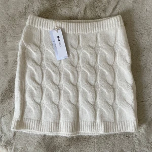 Vit stickad kjol M - Snygg vit stickad kjol med ett flätat mönster. Perfekt för kyligare dagar med sin mysiga och stilrena design. Kjolen har en elastisk midja för bekväm passform.