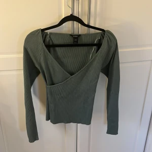 Grön ribbad omlottopp från Lindex  - Snygg grön ribbad omlottopp från Lindex med långa ärmar. Perfekt för en stilren look. Toppen har en v-ringad design och är tillverkad i ett mjukt material.