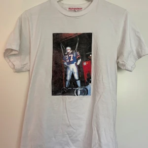 Vit t-shirt med tryck från Richardson - Säljer en vit t-shirt från Richardson med ett coolt tryck av en amerikansk fotbollsspelare på framsidan. T-shirten har en klassisk passform och är kortärmad.