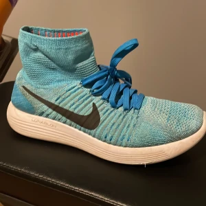 Nike lunarepic i blå  - Snygga och sportiga Nike Flyknit sneakers i en fräsch blå färg. Skorna har en hög ankel och är utrustade med snörning för bästa passform. Den stickade designen ger en lätt och flexibel känsla, perfekt för träning eller vardagsbruk.
