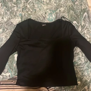 Svart topp från Gina Tricot - Säljer en stilren svart topp från Gina Tricot. Toppen har långa ärmar och en enkel design som passar perfekt till olika tillfällen. Den är gjord i ett mjukt material som känns skönt mot huden.den är lite kroppad