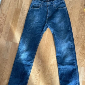 Blå jeans från Armani Jeans - Snygga blå jeans från Armani Jeans med klassisk femficksdesign och knappgylf. De har en diskret logga på bakfickan och en läderpatch med märkesnamnet. Perfekta för en stilren look. Rak modell midja 36 cm (29 tum). Benlängd 80 cm