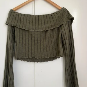 Olivgrön ribbad offshoulder-tröja - Snygg olivgrön offshoulder-tröja med ribbad struktur och långa ärmar. Perfekt för en trendig look med sin croppade design. 