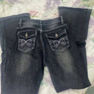 Svarta jeans med broderade bakfickor - Snygga mörkblå jeans med unika broderade detaljer på bakfickorna. De har en klassisk femficksdesign och knappar på ficklocken. Perfekta för en stilren look.