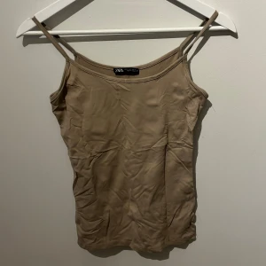 Beiget linne från Zara - Säljer en stilren beige linne från Zara med smala axelband. Perfekt för varma sommardagar eller som ett lager under en kavaj. 