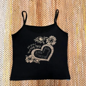 Svart linne med blommigt tryck - Snygg svart linne med smala axelband och ett dekorativt blommigt tryck i form av ett hjärta på framsidan. Perfekt för en avslappnad stil.