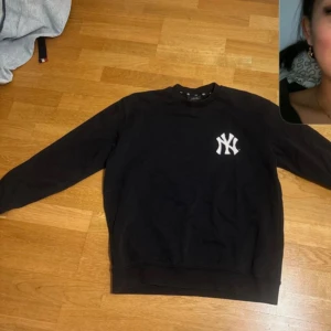 Svart sweatshirt med Yankees-tryck - Säljer en svart sweatshirt från MLB med Yankees-logga på bröstet och texten 'PLAY MLB #YANKEES' på ryggen. Tröjan har långa ärmar och en rund halsringning. Storlek s men väldigt oversized kan lätt passa m.