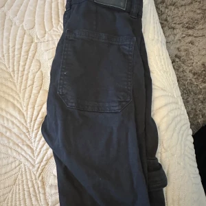 Svarta cargopants med fickdetaljer - Snygga svarta cargopants med praktiska fickor och knappdetaljer. Byxorna har en dragkedja framtill och är perfekta för en avslappnad stil. De har en loose passform och är tillverkade i ett bekvämt material.