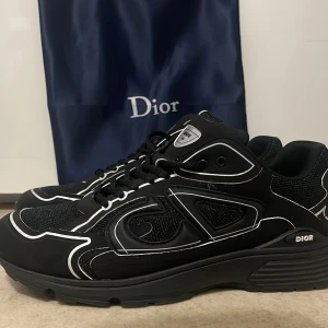 Svarta sneakers från Dior - Snygga svarta sneakers från Dior med vita detaljer och CD-logga på hälen. Skorna har en robust sula och snörning framtill. Perfekta för en stilren look.
