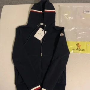 Mörkblå huvtröja från Moncler - Säljer en mörklblå zip tröja från moncler, köptes för lite mindre än 3 månad sen har aldrig använt då den va för liten. Nfc scan funkar och påse och en tag tillkommer. Bara höra av sig om du har några frågor!