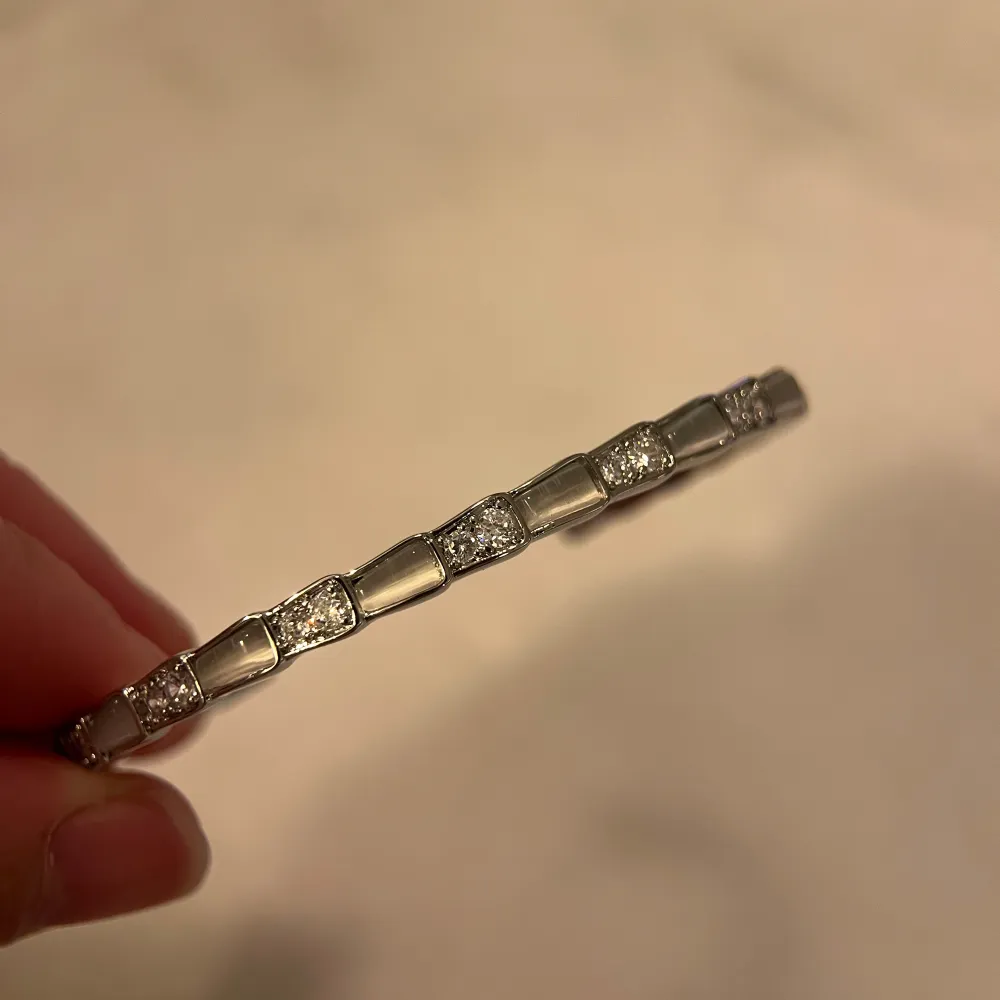 Elegant silverfärgat armband med glittriga detaljer. Armbandet har en stilren design med små fyrkantiga länkar som är dekorerade med gnistrande stenar. Perfekt för att ge en touch av glamour till din outfit.. Asusteet.