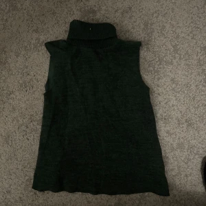 Mörkgrön ärmlös polotröja - Snygg mörkgrön ärmlös polotröja perfekt för lager-på-lager-stil. Den har en hög polokrage som ger en stilren look. Passar utmärkt till både jeans och kjol.