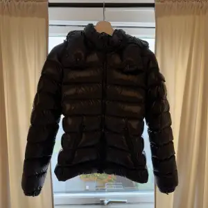 Moncler Maya, svart – storlek 2  Säljer min Moncler Maya i svart, storlek 2. Jackan är i nästan nyskick, då jag har använt den max fem gånger. Inga skador, fläckar eller tecken på slitage – ser i princip ut som ny. Jackan har en luva som går att ta både av och på.  En stilren och lyxig dunjacka som är både lättviktig och varm, perfekt för kyliga dagar. Säljes endast eftersom jag inte använder den.  Nypris ligger på 15 000 + kr Pris kan diskuteras.