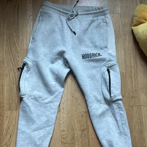 Grå mjukisbyxor från Hoodrich - Snygga grå mjukisbyxor från Hoodrich med snörning i midjan och dragkedjor på benen. Perfekta för en avslappnad stil.