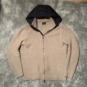 Massimo dutti cardigan - Säljer en snygg beige stickad cardigan från Massimo Dutti. Tröjan har en dragkedja framtill och en quiltad huva i svart. Perfekt för kyliga dagar med sin stilrena design och bekväma passform. Storlek M och passar runt 180! INGA BYTEN!