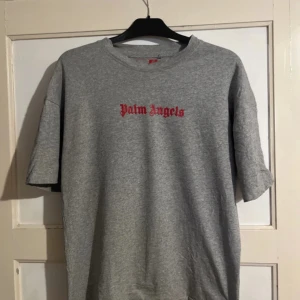 Grå t-shirt från Palm Angels - Snygg grå t-shirt från Palm Angels med röd text både fram och bak. Perfekt för en avslappnad stil. Tillverkad i mjukt material för extra komfort.