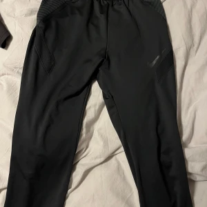 Svarta träningsbyxor från Nike - Snygga svarta träningsbyxor från Nike med elastisk midja och dragsko. Byxorna har en diskret Nike-logga på benet och praktiska sidofickor. Perfekta för träning eller en avslappnad dag.