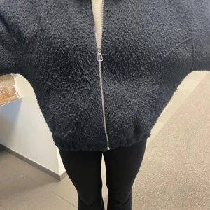 Svart teddyjacka med dragkedja - Mysig svart teddyjacka med dragkedja framtill. Jackan har en oversized passform och långa ärmar, perfekt för kyliga dagar. Den fluffiga texturen ger en trendig look.