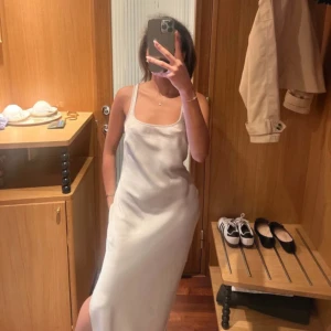 Silver somsøe somsøe balklänning  - Elegant silvrig klänning i silkesmaterial med urringning. Perfekt för bal eller när man vill klä upp sig extra! Skiftar i lite champagne toner🩰