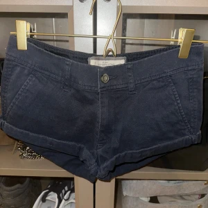 Svarta low waist shorts från Abercrombie & Fitch - Snygga svarta shorts från Abercrombie & Fitch med knapp och dragkedja framtill. De har två framfickor och två bakfickor, samt en liten broderad logga på baksidan. Perfekta för en avslappnad stil. Low waist 