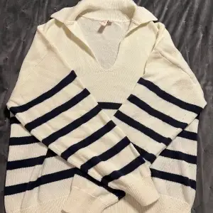Säljer en stilren vit tröja från Nelly med marinblå ränder. Tröjan har en v-ringad krage och långa ärmar, perfekt för en avslappnad look. Den är tillverkad i ett mjukt material som känns skönt mot huden.