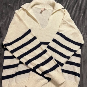 Vit och marinblå randig tröja från Nelly - Säljer en stilren vit tröja från Nelly med marinblå ränder. Tröjan har en v-ringad krage och långa ärmar, perfekt för en avslappnad look. Den är tillverkad i ett mjukt material som känns skönt mot huden.