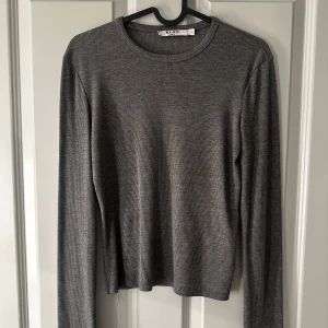 Grå ribbad tröja  - Säljer en stilren grå ribbad tröja från NA-KD. Tröjan har långa ärmar och en klassisk rund halsringning. Perfekt för lager-på-lager eller att bära som den är. Passar till många olika stilar och tillfällen.