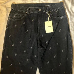 Mörkgrå jeans från Axel Arigato - Snygga mörkgrå jeans från Axel Arigato med ett diskret mönster av bokstäver. Byxorna har en klassisk femficksdesign och knappgylf. Aldrig använda och finns ej kvar. Unisex