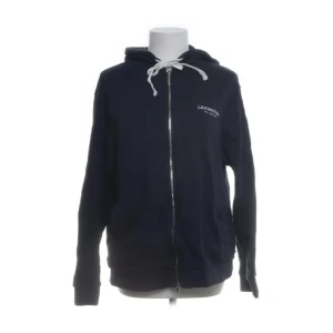 Mörkblå hoodie från Lexington - Säljer en snygg mörkblå hoodie från Lexington med dragkedja och vit snörning i luvan. Tillverkad i 100% bomull för en bekväm känsla. Perfekt för en avslappnad stil.