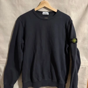 Svart sweatshirt från Stone Island Junior - Säljer en stilren svart sweatshirt från Stone Island Junior. Tröjan har långa ärmar och en rund halsringning. Den ikoniska logotypen finns på ärmen. Perfekt för en avslappnad stil. Storlek 176/xs