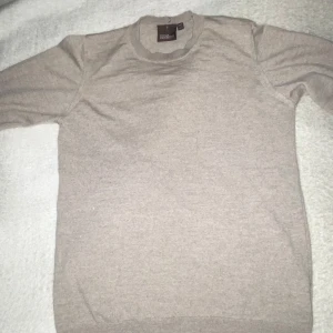 Beige ulltröja från Oscar Jacobson - Tjena säljer en stilren beige tröja från Oscar Jacobson, tillverkad i 100% merinoull. Tröjan har en klassisk rund hals och långa ärmar, perfekt för kyligare dagar. Modellen är 185cm och nypris är 1500kr. Tillverkad i Italien, vilket garanterar hög kvalitet och komfort. Priset är långt ifrån hugget i sten.