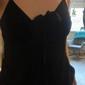 Svart topp från Gina Tricot - Säljer en stilren svart topp från Gina Tricot. Toppen har en elegant design med smala axelband och en knytdetalj framtill. Perfekt för en chic look.