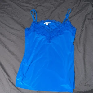 Blått spets linne från New Yorker  -  Blått spets linne från New Yorker. Linnet har smala axelband och en v-ringad design. Aldrig använd.