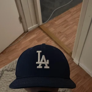 Blå keps med LA-logga - Snygg blå keps från New Era med LA-logga framtill. Justerbar passform baktill för optimal komfort. Perfekt för en avslappnad stil.