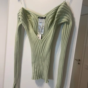 Ljusgrön ribbad topp från Gina Tricot - Snygg ljusgrön ribbad topp från Gina Tricot med en djup v-ringning. Toppen har långa ärmar och en figurnära passform som framhäver silhuetten. Perfekt för en stilren look.