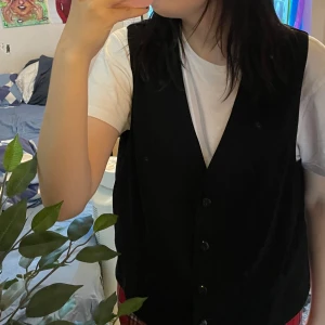 Svart väst med knappar - Säljer en stilren svart väst med knappar framtill. Perfekt för att lägga till en touch av elegans till din outfit. Västen är i bra skick och passar till både vardag och fest. vet inte vilken storlek den är då jag fick den men passar mig som normal har S-M