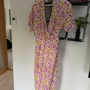 Blommig klänning från Bik Bok - Säljer en superfin blommig klänning från Bik Bok i storlek S. Den har en vacker mix av rosa och gula blommor på en vit bakgrund. Klänningen är kortärmad och har en djup v-ringning. Perfekt för sommarens alla fester! Den har en dragkedja i ryggen för enkel påklädning.