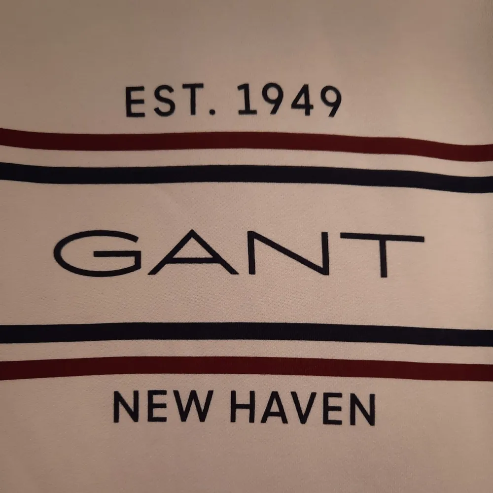 Säljer en stilren vit sweatshirt från GANT med tryck 'EST. 1949' och 'NEW HAVEN' i svart. Tröjan har ett klassiskt snitt med långa ärmar och ribbade muddar. Perfekt för en avslappnad och snygg look!. Tröjor & Koftor.