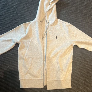 Ralph Lauren luvtröja med dragkedja - Mycket gott skick. Endast använd en gång!  Säljer en luvtröja med dragkedja av märket Ralph Lauren på grund av att den ej passade min storlek.  Skickas tvättad och välpacketerad med antigen Instabox eller Postnord