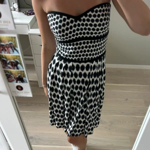 Svartvit prickig klänning från Mango - Säljer en superfin svartvit klänning från Mango i storlek XS. Den är axelbandslös och har ett prickigt mönster. Perfekt för sommarens fester eller en dag på stan. Klänningen har en tight passform upptill och en lite lösare kjol!