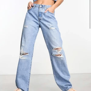 Blå slitna jeans - Säljer ett par snygga blå jeans med slitningar. De är högmidjade och har en avslappnad, wide fit. Perfekta för en casual look och passar till nästan allt. Jeansen har klassiska fickor och knappar i midjan.