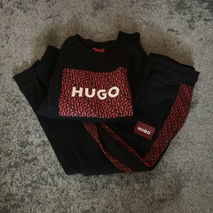 Svart tröja från Hugo - Säljer ett snyggt sett från Hugo med ett coolt rött och svart mönster där det står 'HUGO'. settet är perfekt för en avslappnad stil. Den är i nyskick och passar perfekt för både vardag och om fest. storlek xs på tröjan och s på byxorna. Skicka ett meddelande om du är intresserad!