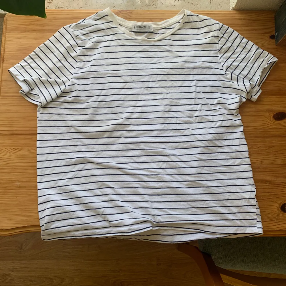 Säljer en klassisk vit och svart randig t-shirt från Stradivarius. Den är i storlek M. Perfekt för vardagsbruk och kan lätt matchas med jeans eller shorts. T-shirten är i bomull och har korta ärmar. I använt skick.. T-shirts.